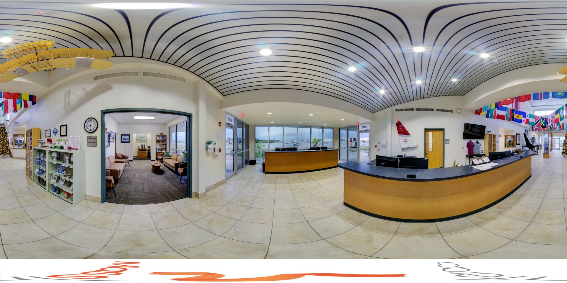 Panoramic view of lobby filled with numerous desks, while national flags and airplane models hang from the ceiling